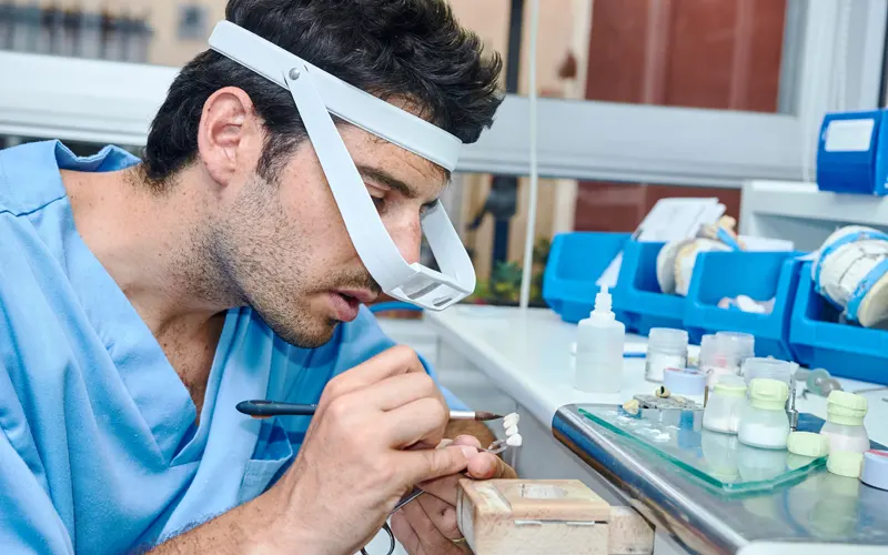 Eine junger Zahntechniker im Labor beim Colorieren einer Krone